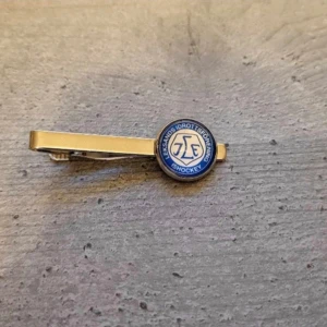 Gul slipsnål med ishockeymotiv Leksand - Snygg gul slipsnål med ett runt emblem i blått och vitt som har ett ishockeymotiv. Perfekt för den sportintresserade som vill lägga till en personlig touch till sin outfit. Passar både till vardag och festliga tillfällen.