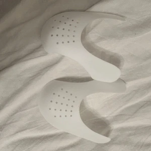 Vita skoinlägg(creesskydd)  - Säljer ett par vita skoinlägg som är perfekta för att hålla formen på dina sneakers. De är gjorda av ett flexibelt material med små hål för ventilation. Perfekt för att förhindra veck och hålla skorna fräscha längre.