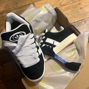 Adidas campus 00 - Säljer ett par snygga svarta och vita Adidas sneakers i nytt skick. kommer med extra svarta skosnören. Levereras i originalkartong.