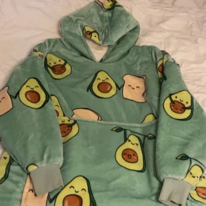 Grön Oodie med avokadotryck - Supermysig och oversized grön Oodie med gulligt avokado- och brödtryck. I original förpackning endast använd 2-3 gånger. Perfekt för kalla dagar när du bara vill mysa hemma. Den är gjord av mjuk fleece och har en stor huva.
