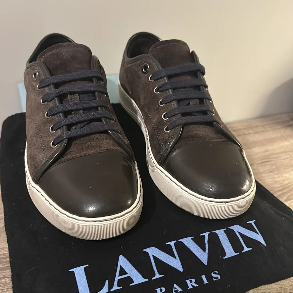 Säljer ett par snygga bruna sneakers från Lanvin i bra skick. Skorna har en stilren design med mocka och skinn, samt blåa snören. Perfekta för både vardag och fest! Storlek 42. Priset kan diskuteras. Har tyvärr inte kvitto, men jag har dust bag och box.. Skor.