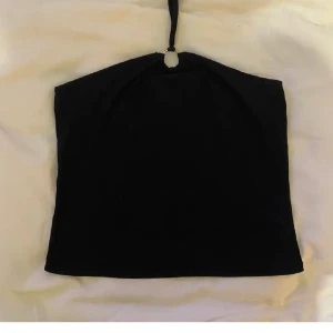 Svart halter  topp - Snygg svart halter topp med en enkel design. Perfekt för en utekväll eller fest. Den har en smal axelrem som knyts i nacken, vilket ger en stilren look. Materialet verkar vara mjukt och stretchigt för en bekväm passform.