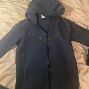 Mörkblå nike teech - Säljer en mörkblå Nike teech i mycket bra skick. Den har en dragkedja framtill och en stilren design med diskreta detaljer. Perfekt för höst och vår, och funkar lika bra till träning som till vardags. Storleken är normal och materialet känns mjukt och bekvämt.