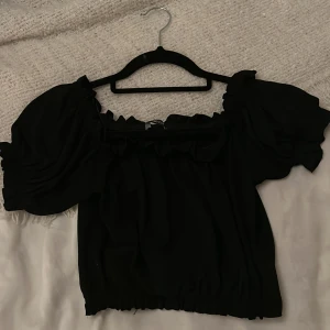 Svart offshoulder topp - Säljer en snygg svart offshoulder topp med puffiga ärmar. Toppen har en elastisk kant vid axlarna och ärmarna, vilket ger en bekväm passform. Perfekt för en utekväll eller fest! 🖤