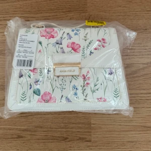 Blommig handväska från Anna Field - Säljer en superfin handväska från Anna Field i vitt med ett vackert blommönster. Väskan är i nytt skick och har en elegant design med en guldfärgad detalj framtill. Perfekt för vår och sommar! 🌸