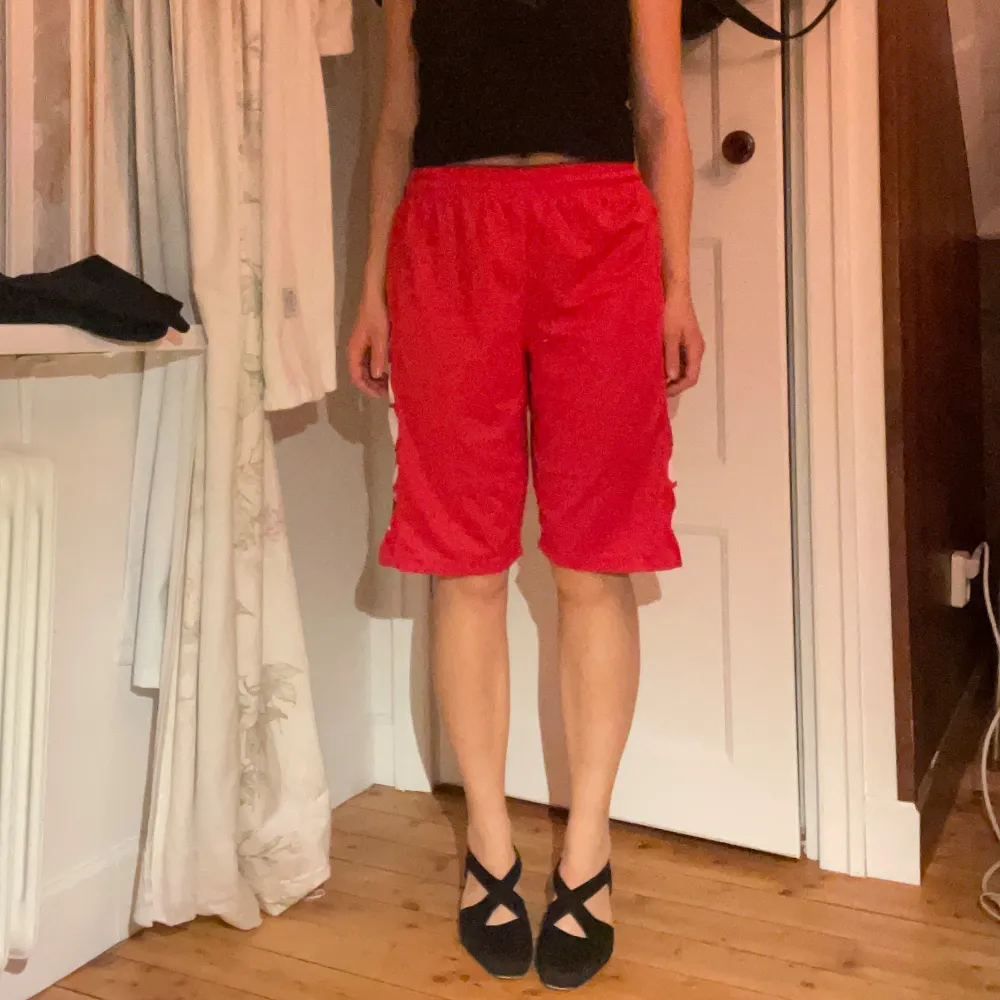 Säljer ett par röda shorts i mycket bra skick. De har en loose passform och är perfekta för sommaren. Shortsen har vita detaljer på sidan som ger en sportig look. Perfekta för både träning och avslappnade dagar. Midjan är elastisk för extra komfort.. Shorts.