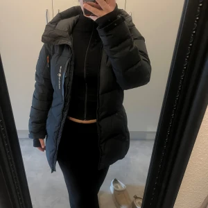 Svart dunjacka från Sail Racing - Säljer en svart dunjacka från Sail Racing i mycket bra skick. Jackan är perfekt för kalla vinterdagar och har en snygg och funktionell design med dragkedja och hög krage. Den har en cool patch på ärmen med 'Sail Antarctica Expedition'. Kvitto finns, köpt för 3499kr