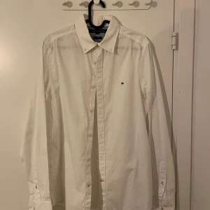 Vit skjorta från Tommy Hilfiger - Säljer en klassisk vit skjorta från Tommy Hilfiger i storlek S. Skjortan har en stilren design med långa ärmar och knappar framtill. Perfekt för både vardag och festliga tillfällen. Den är i mycket bra skick och har en normal passform. Passar perfekt till både jeans och kostymbyxor!