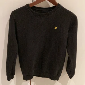 Svart tröja från Lyle & Scott Junior - Säljer en stilren svart tröja från Lyle & Scott Junior. Den har en liten gul logga på bröstet och är perfekt för både vardag och skola. Tröjan är i mycket bra skick och har långa ärmar. Passar perfekt för höst och vinter!