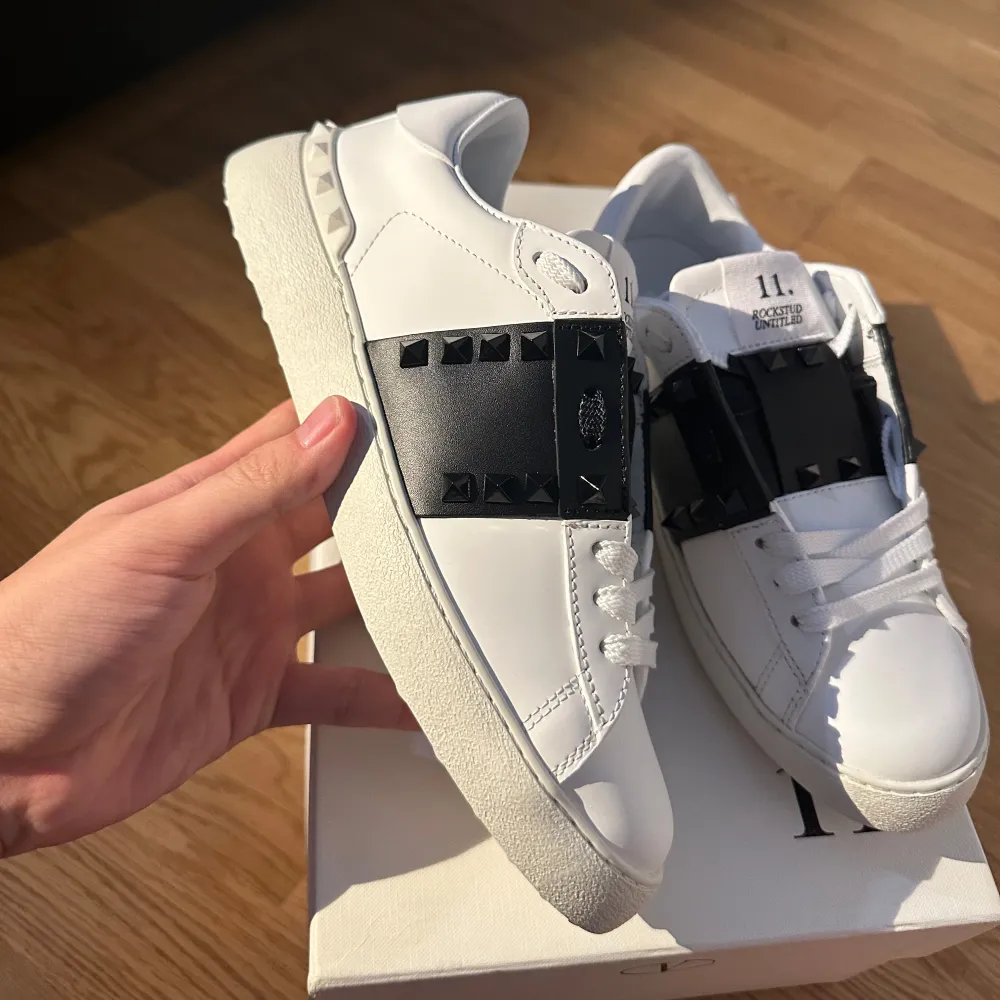 Säljer ett par snygga Valentino Open sneakers i vitt skinn med svarta detaljer. Skorna har coola nitar på sidorna och en klassisk snörning. Perfekta för både vardag och fest! De är i nytt skick och kommer med originalkartong.. Skor.