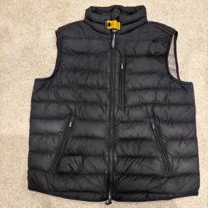 Svart dunväst från Parajumpers - Säljer en svart dunväst från Parajumpers i mycket bra skick. Västen har en dragkedja framtill och två praktiska fickor med dragkedja. Den är quiltad och har en snygg broderad logga på baksidan. Perfekt för höst och vår!