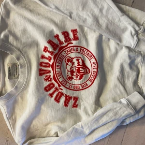 Vit sweatshirt från Zadig & Voltaire - Säljer en snygg vit sweatshirt från Zadig & Voltaire med rött tryck på framsidan. Pytteliten grå fläck längst ner längs mudden fram (zooma första bilden)