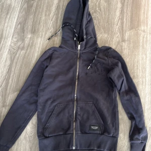 Svart hoodie från Peak Performance - Säljer en svart hoodie från Peak Performance i bra skick. Den har en dragkedja framtill och en justerbar huva med snören. Perfekt för höst och vinter, med ribbade muddar vid ärmslut och nederkant. Superbekväm och stilren!