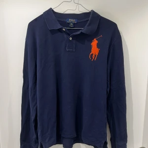 Mörkblå pikétröja från Ralph Lauren - Säljer en snygg mörkblå pikétröja från Ralph Lauren i storlek M/L beroende på längd. Tröjan har en stor logga på bröstet och en siffra '3' på ärmen. Passar perfekt med en vit t-shirt under. Skicket är bra 8/10. Hör gärna av dig vid funderingar! 