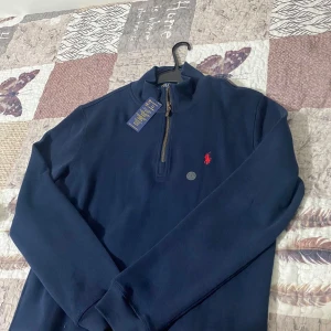 Mörkblå tröja från Polo Ralph Lauren - Säljer en snygg mörkblå tröja från Polo Ralph Lauren. Den har en dragkedja vid halsen och det klassiska röda Polo-logotypen på bröstet. Perfekt för både vardag och lite finare tillfällen. Tröjan är i nyskick och redo att bäras! Priset kan diskuteras