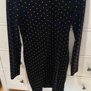 Svart klänning med prickar - Säljer en superfin svart klänning med små detaljer över hela tyget. Den är långärmad och perfekt för en festlig kväll. Klänningen har en tight passform som framhäver figuren. Materialet känns mjukt och bekvämt mot huden. Helt ny 