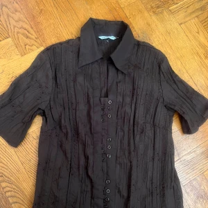 Brunt blus med knappar - Säljer en elegant brunt blus med knappar framtill. Blusen har en klassisk krage och trekvartsärmar. . Perfekt för både vardag och fest!