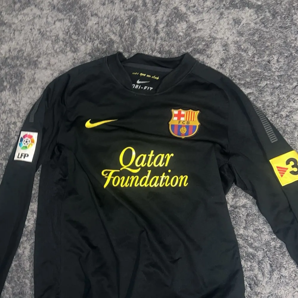 Säljer en svart långärmad FC Barcelona tröja från Nike. Tröjan har klubbens emblem på bröstet och Qatar Foundation som sponsor tryckt i gult på framsidan. Den är i Dri-Fit material och har LFP-märket på ärmen. Perfekt för alla Barca-fans! 💛Kunden står för frakten (pris kan diskuteras). T-shirts.