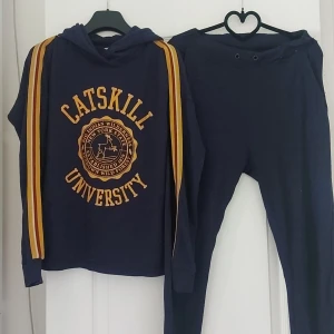 Mörkblå hoodie med byxor från Catskill University - Säljer en snygg och bekväm mörkblå hoodie med matchande byxor( Catskill University).. Hoodien har gula ränder längs ärmarna och en stor Catskill University-logga på bröstet. Perfekt för en avslappnad dag, hemmamys eller träning. Setet är i bra skick trots att snören på byxorna har lossnat men den elastiska håller den på plats ändå.  Skönt avslappnad material. priset för båda delarna. Passa på att fynda ;)