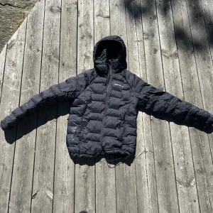 Svart dunjacka från Peak Performance - Säljer en svart dunjacka från Peak Performance. Jackan är långärmad och har en dragkedja framtill. Den är perfekt för kalla dagar och håller dig varm och bekväm. Jackan har en huva och är i mycket bra skick. Perfekt för vintern!