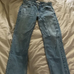 Blå jeansbyxor från Zara - Säljer ett par snygga blå jeansbyxor från Zara i storlek 34. De är i bra skick och har en klassisk straight fit. Perfekta för vardagsbruk och kan matchas med nästan vad som helst. De har en dragkedja och knappar framtill samt fickor både fram och bak. Materialet är slitstarkt och bekvämt.