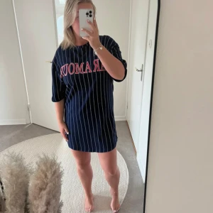 Svart och vit randig t-shirtklänning - Säljer en marinblå och vit randig t-shirtklänning med texten 'ARMOUR' i rött på bröstet. Den är oversized och har korta ärmar. Perfekt för en avslappnad stil eller som en bekväm vardagsoutfit. 🖤