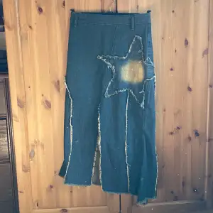 Säljer en supercool jeanskjol med en stor stjärndetalj på framsidan. Kjolen är lång och har en rå kant som ger den en edgy look. Den har också en dragkedja på baksidan och slitdetaljer längs sidorna. Perfekt för en avslappnad men ändå stilren outfit!