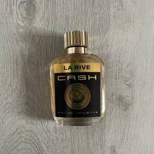 La Rive Cash Eau de Toilette 100ml  - Säljer en elegant flaska av La Rive Cash Eau de Toilette. Flaskan har en stilren design med en svart och guldig etikett och ett matchande guldlock. Perfekt för den som söker en sofistikerad doftupplevelse. 100ml 