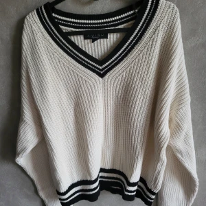 Vit stickad tröja från Amisu - Säljer en snygg vit stickad tröja från Amisu med svarta ränder vid v-ringningen och nederkanten. Tröjan har en avslappnad passform och långa ärmar, perfekt för kyligare dagar. Storlek XL men passar S/M som oversize. 