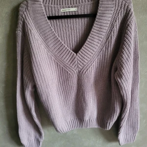 Ljuslila stickad tröja från House Brand - Mysig ljuslila stickad tröja från House Brand med en djup v-ringning. Tröjan har långa ärmar och ribbade kanter som ger en stilren look. Perfekt för kyliga dagar!