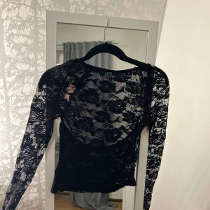 Svart spetsblus - Trendig elegant svart spetsblus med långärmad design. Blusen har ett vackert blommigt mönster och är perfekt för en stilfull look. .