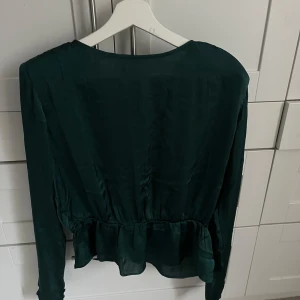 Grön blus med knytning - Snygg grön blus med v-ringning och knytning i ryggen. Blusen har långa ärmar och en volangdetalj i nederkanten. Aldrig använd💕