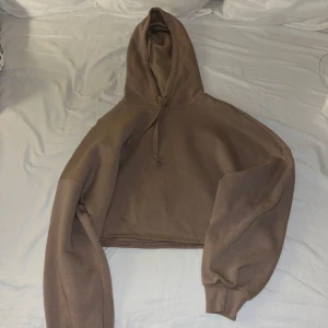 Brun croppad hoodie från Gina Tricot - Säljer en brun croppad hoodie från Gina Tricot. Den har en mysig huva och långa ärmar med ribbade muddar. Perfekt för en avslappnad stil.