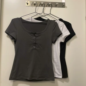 T-shirt i tre färger med knappar - Säljer tre t-shirts i svart, grått och vitt. Perfekt för att ge sin outfit lite mer spice! Köpte dessa för tre månader sedan, men han byt klädstil nu så jag använder de knappt. 