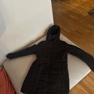 Svart lång dunjacka med luva  - Säljer en svart lång dunjacka med luva. Den är helt ny och köpte den för 700kr. Den skulle vara perfekt för mig fast den är tyvärr för stor. 