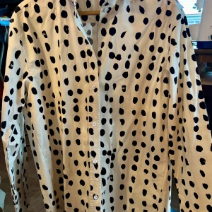 Vit och svart prickig skjorta från Carin Wester - Snygg vit skjorta med svarta prickar från Carin Wester. Skjortan har långa ärmar och knappar framtill. Perfekt för att ge en stilren touch till din outfit.
