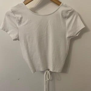Vit kortärmad topp från Gina Tricot - Säljer en vit kortärmad topp från Gina Tricot med knytning framtill och en snygg omlott-design. Perfekt för sommardagar och kan enkelt matchas med olika outfits. Oanvänd