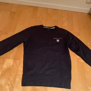 Marinblå tröja från GANT - Snygg svart tröja från GANT med broderad logga och emblem på bröstet. Perfekt för en stilren look. Tröjan är i bra skick utan några sorts skavanker eller märken. Kom pv om ni undrar någonting! Pris kan diskuteras!😃