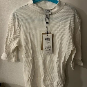 Vit ribbad tröja från Aware - Säljer en stilren vit ribbad tröja från Aware. Tröjan har trekvartsärmar och en hög krage, perfekt för en minimalistisk look. Passar bra till både jeans och kjol. 🌟