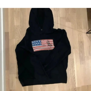 Svart hoodie med amerikansk flagga - Snygg svart hoodie med en patch av den amerikanska flaggan och en häst på framsidan. Skit snygg tröja och du kan ha den till allt.