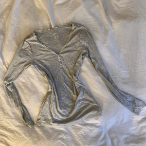 Grå långärmad topp från Esmara - Säljer en stilren grå långärmad topp från Esmara. Toppen har en v-ringad design med spetsdetaljer och knappar framtill. Perfekt för en avslappnad look.