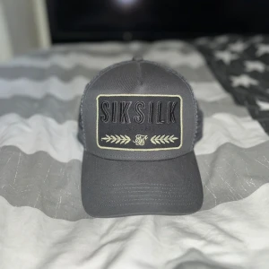 Grå keps från SikSilk - Snygg grå keps från SikSilk med broderad logga framtill. Perfekt för en avslappnad stil. Justerbar passform för optimal komfort.