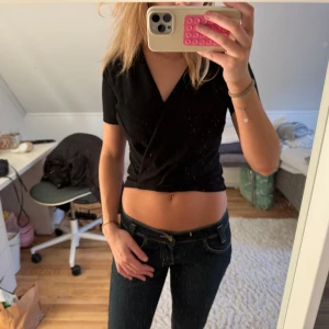 Svart omlottopp - Säljer en stilren svart omlottopp med korta ärmar. Toppen är croppad och har en v-ringad design som ger en trendig look. Perfekt för att matcha med jeans eller kjol.