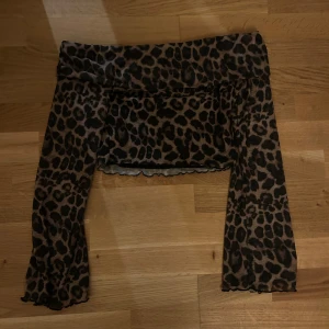 Leopardmönstrad offshoulder topp - Trendig offshoulder topp med leopardmönster. Perfekt för en djärv look, med långa ärmar och en smickrande passform. Ett måste för garderoben!