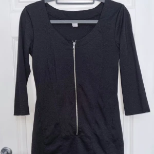 Svart klänning med dragkedja - Snygg svart klänning från VILA med en framträdande dragkedja framtill. Klänningen har trekvartsärmar och en figurnära passform som ger en stilren look. Perfekt för både vardag och festliga tillfällen.