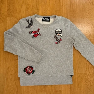 Grå sweater - Karl Lagerfeld - Grå tröja från Karl Lagerfeld med påsydda detaljer. Köpt på Arkivet 