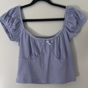 Snygg topp med rosett - Finaste ljusblå/lila toppen med korta puffärmar o en söt liten rosett framtill. Toppen har spets längs urringningen o är perfekt inför sommaren!! Lapp saknas men uppskattas till S(m) 💌