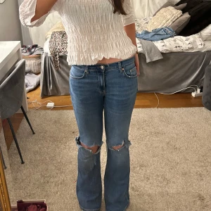 Blå jeans med slitningar från Gina Tricot - Säljer ett par blå lågmidjade bootcut jeans från Gina Tricot med slitningar på knäna. 