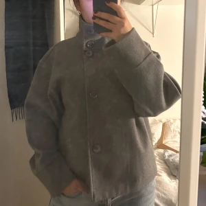 Grå kappa med knappar - Säljer en stilren grå kappa i en kortare modell med stora knappar framtill. Jackan har en hög krage och långa ärmar, men kragen kan även vikas ned för en mer klassisk look. Tidlös design! Köpt på arkivet i Stockholm men saknar tags så vet tyvärr inte märket. Känns som en hög kvalitativ jacka och arkivet säljer ju mestadels exklusiva märken! Köpt för 900kr men har aldrig kommit till användning, pris pga att jag inte vet märke