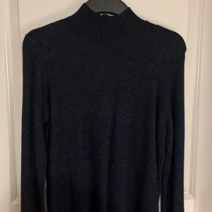 Mörkblå stickad polotröja - Snygg och stilren mörkblå stickad polotröja med långa ärmar. Perfekt för kyliga dagar och passar till många olika outfits. Ribbstickad krage och muddar ger en klassisk look.